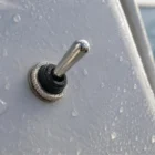Marine toggle switch installed on boat panel, metal parts visible, water spray