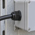 Black nylon cable gland mounted through an enclosure wall sealing a cable
